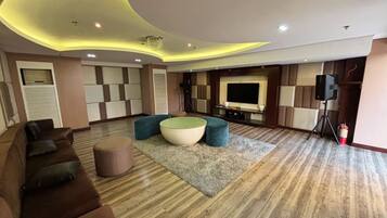 A modern living room with a curved ceiling, a large flat-screen TV, a sofa, ottomans, and a wooden floor.