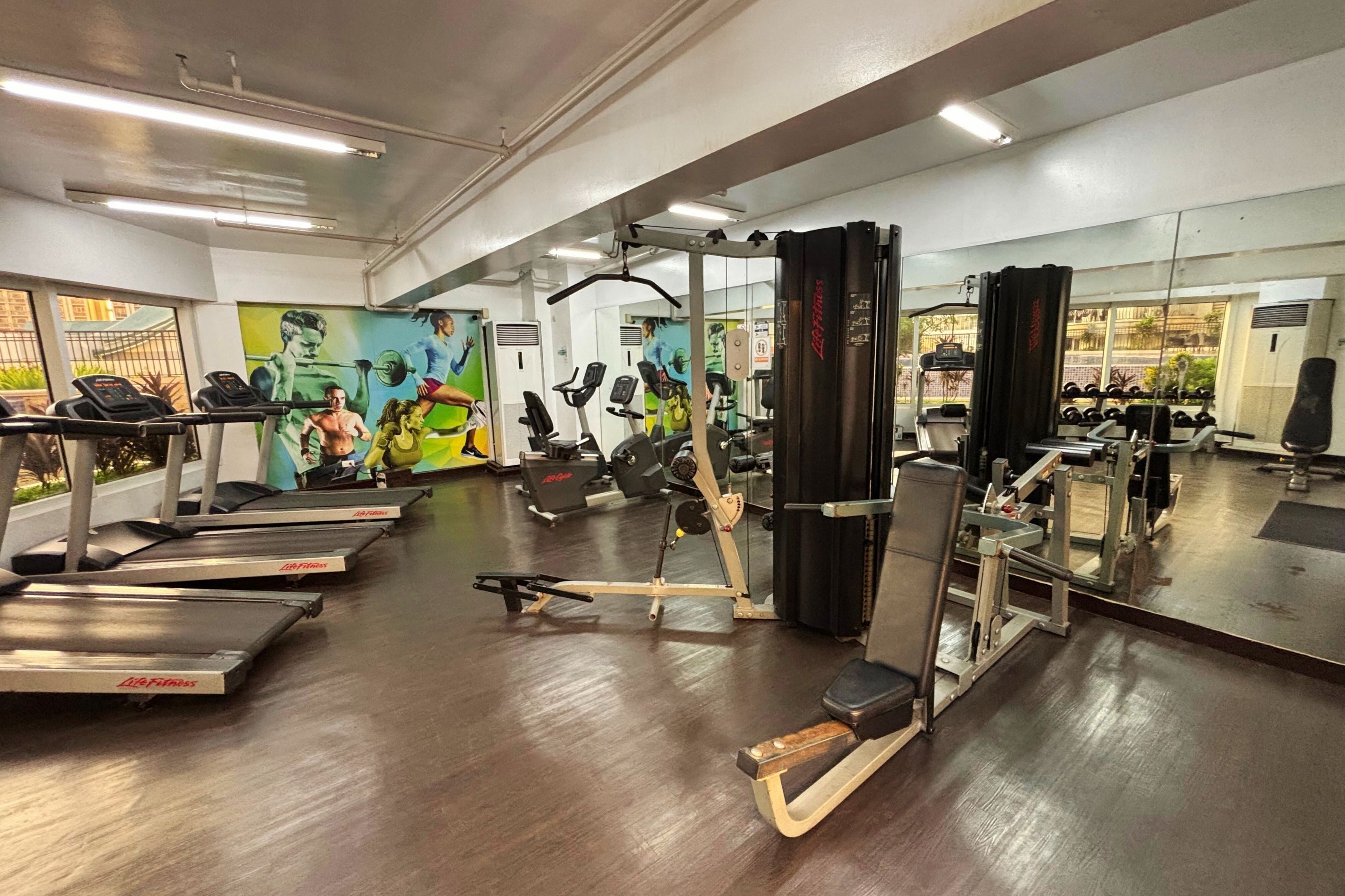 Un gimnasio con cintas de correr, máquinas de pesas y un muro de espejos.