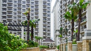 A modern residential building with multiple balconies, a central courtyard with palm trees, and a covered seating area. - Extremeli Suites (Parañaque)