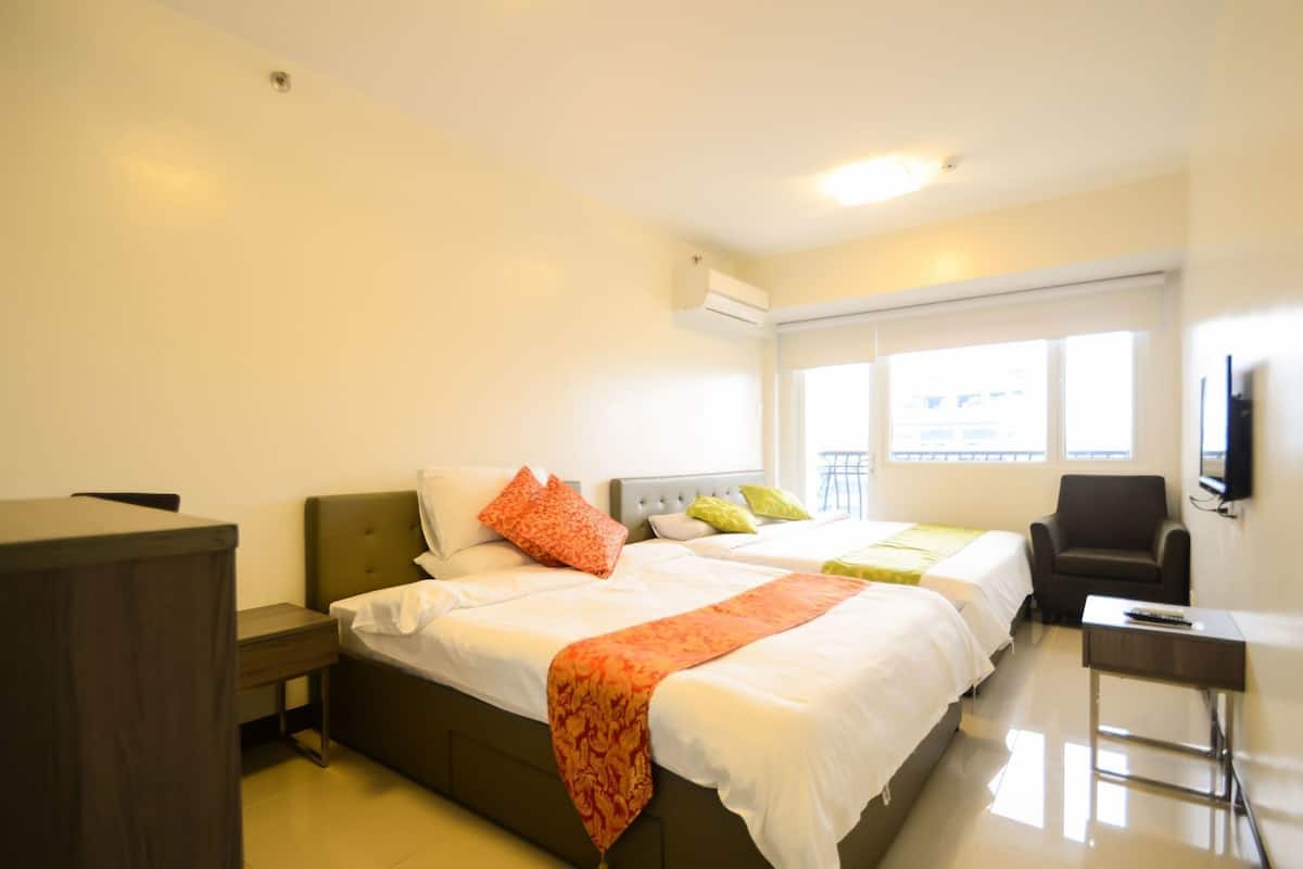 A hotel room with two beds, a desk, a chair, and a TV.