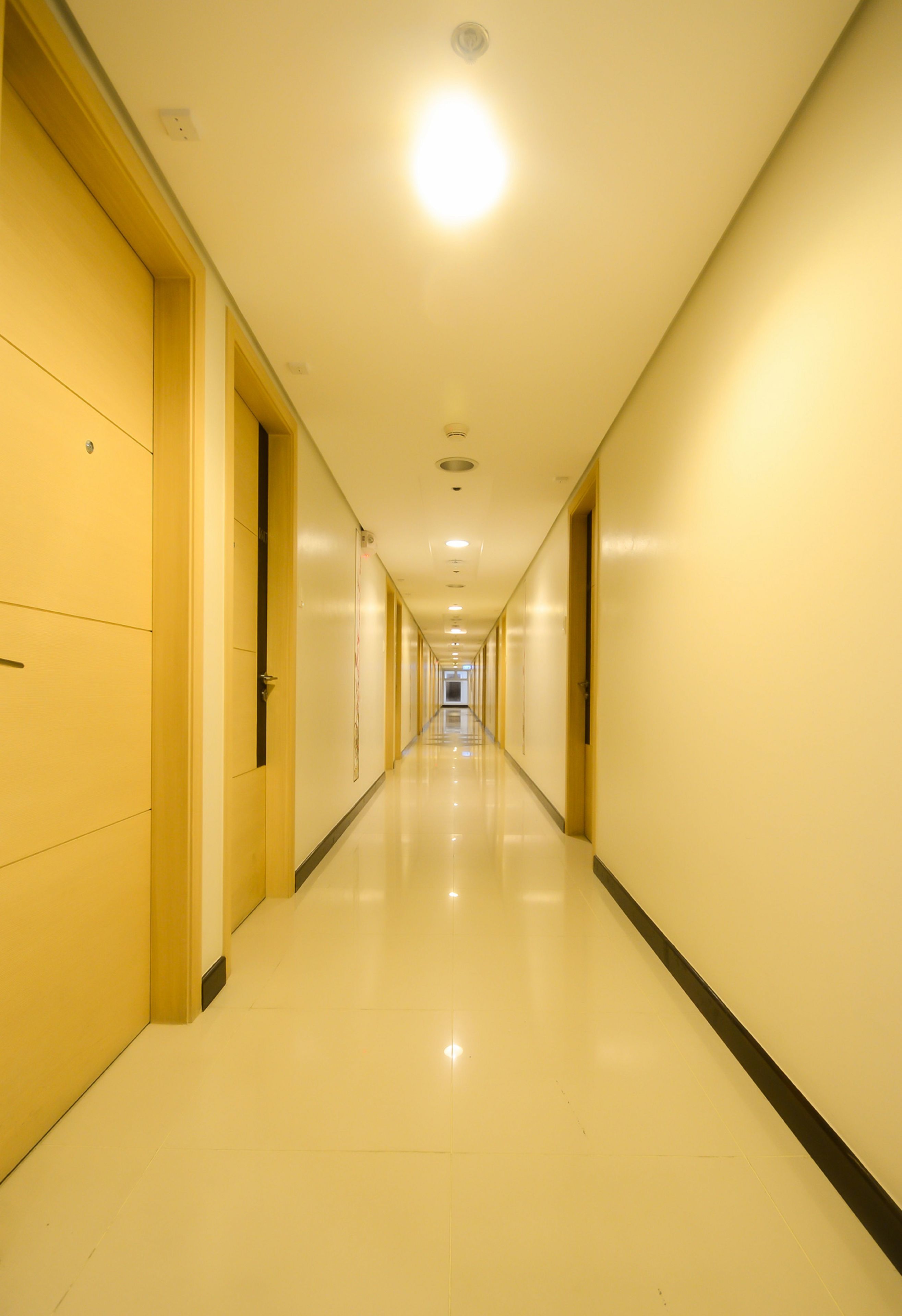 Corredor longo e estreito de hotel, com portas em ambos os lados, que se estende até o final.