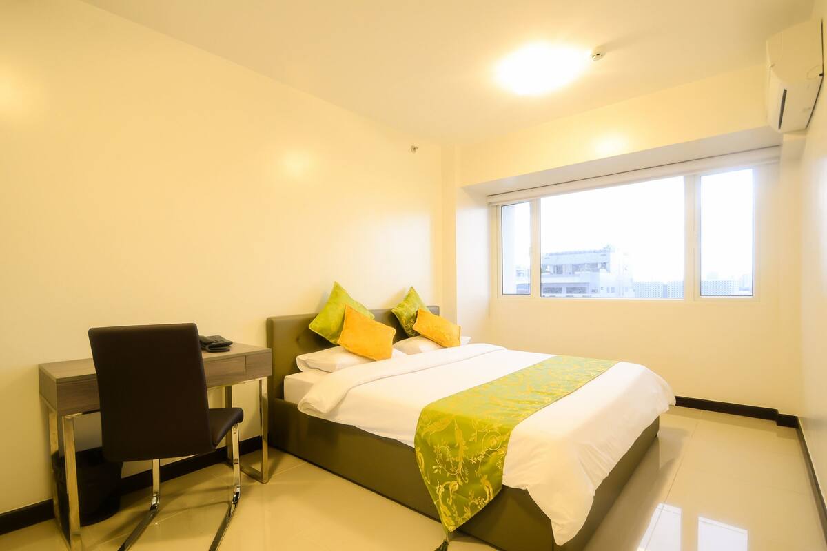 A hotel room with a bed, a desk, a chair, and a window.