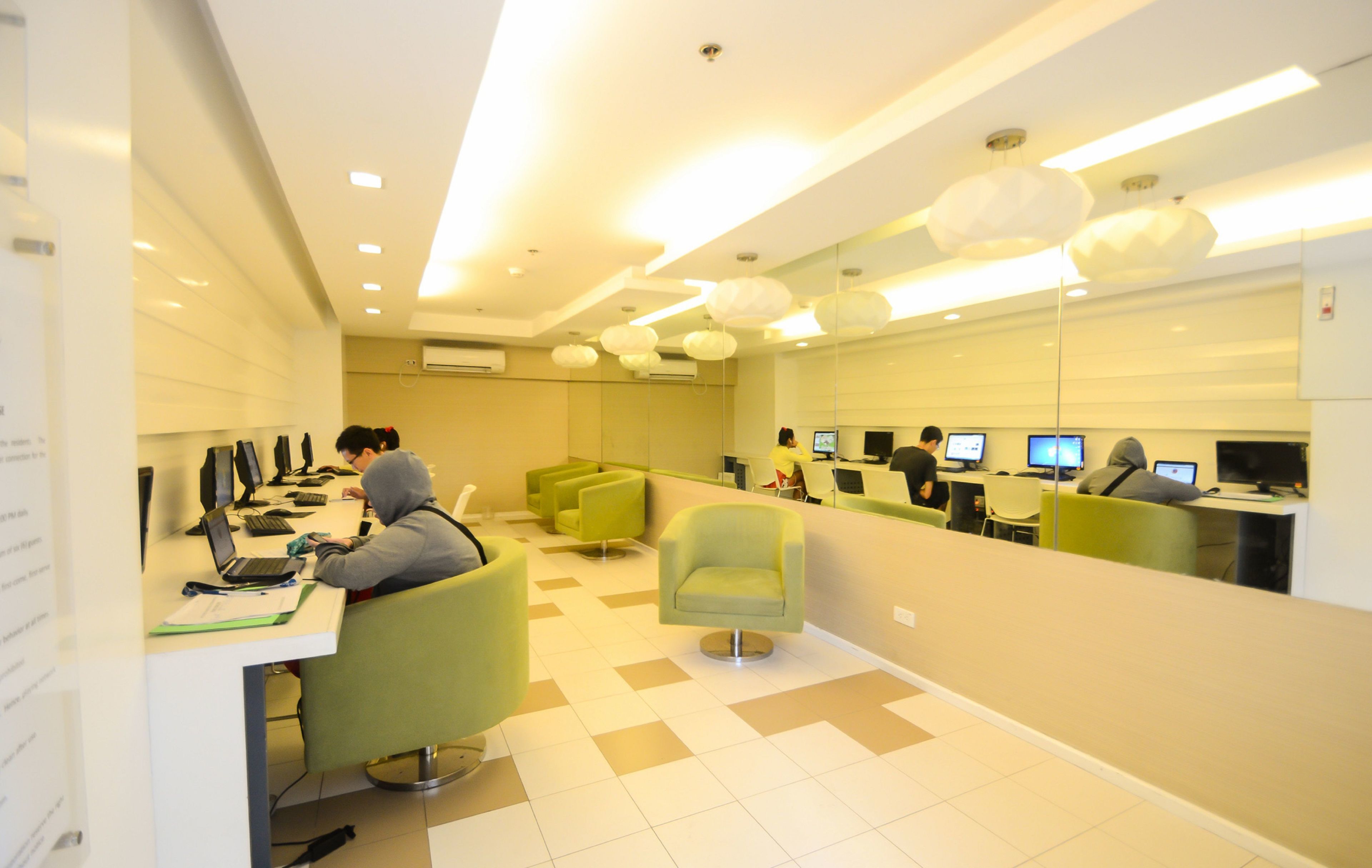 Ein modernes Büro mit mehreren Arbeitsplätzen, grünen Stühlen und einer großen Spiegelwand.