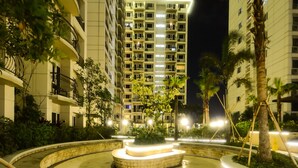 A well-lit outdoor area with a curved pathway, palm trees, and a high-rise building with balconies. - Extremeli Suites (Parañaque)