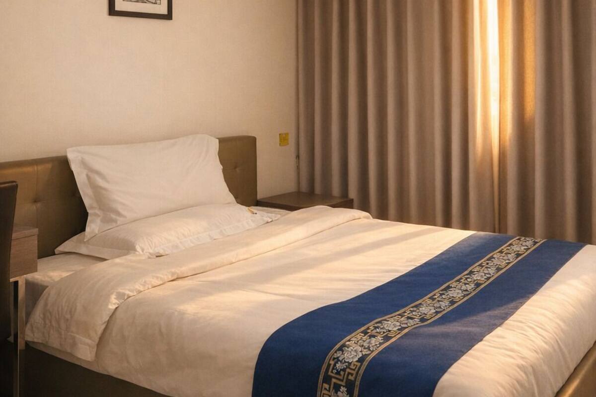 A hotel room with a bed, an air conditioning unit, a framed picture on the wall, and a window with curtains.