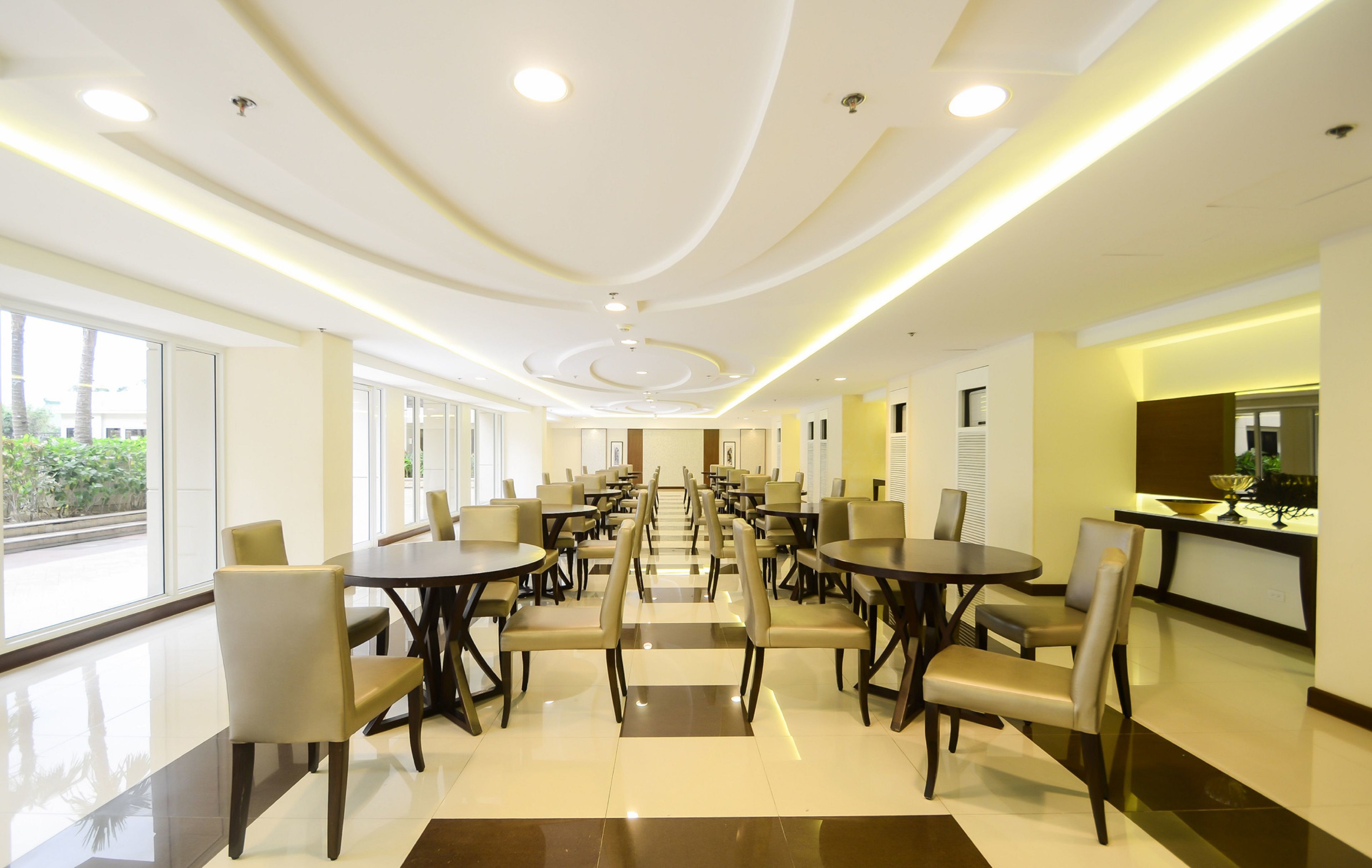 A spacious dining area with multiple tables and chairs, large windows, and a modern ceiling design.