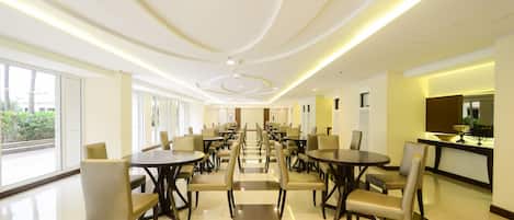 A spacious dining area with multiple tables and chairs, large windows, and a modern ceiling design.