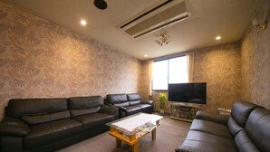 A living room with a sofa set, a coffee table, a flat-screen TV, and patterned wallpaper. - Hotel Nagisa (Beppu)