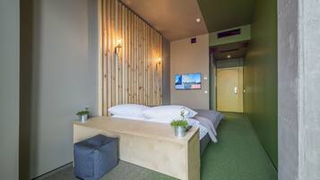 Una habitación moderna con una cama, un escritorio y un televisor montado en la pared.