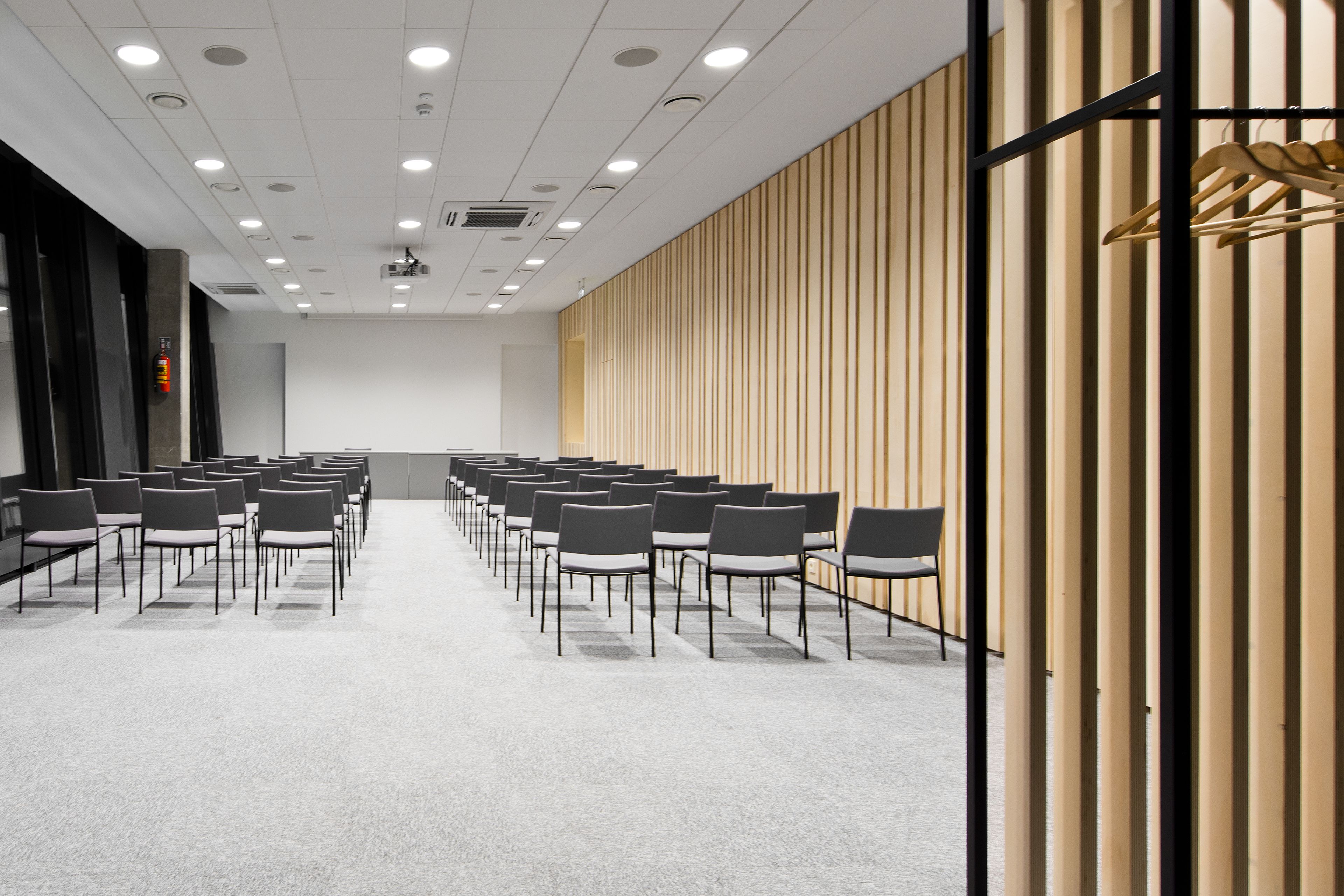 A conference room with rows of chairs, a wooden panel wall, and a ceiling with recessed lighting.