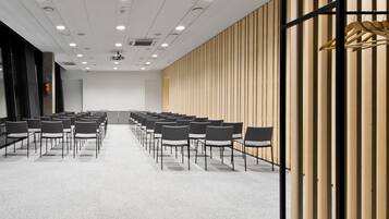 A conference room with rows of chairs, a wooden panel wall, and a ceiling with recessed lighting.