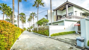 A modern residential street with a paved walkway, palm trees, and a white building with a balcony. - Sotis Villa Canggu (Canggu)
