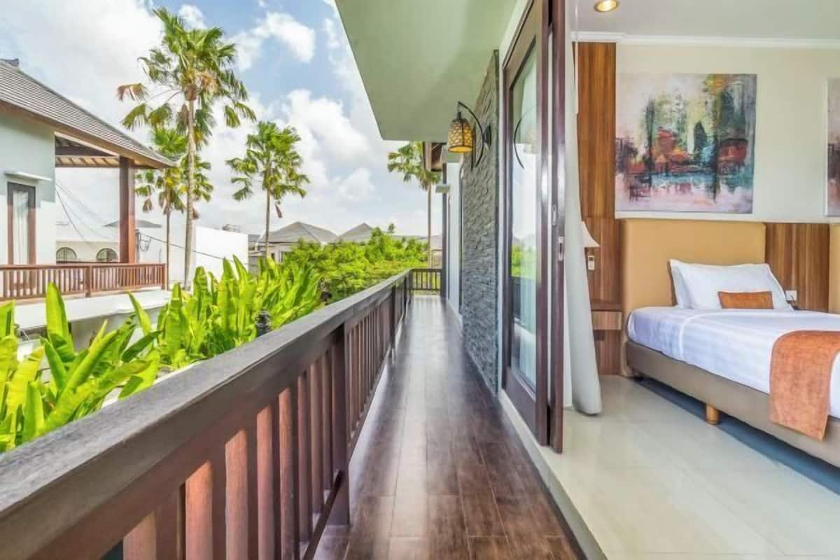 A balcony with a wooden railing, a bed with white bedding, and a painting on the wall.