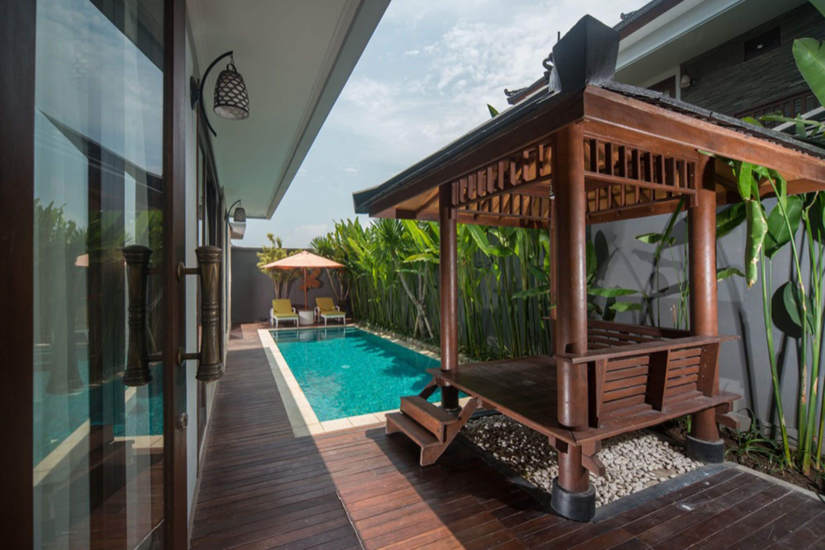 Une terrasse en bois avec une piscine, entourée de plantes tropicales et agrémentée d’une pergola.