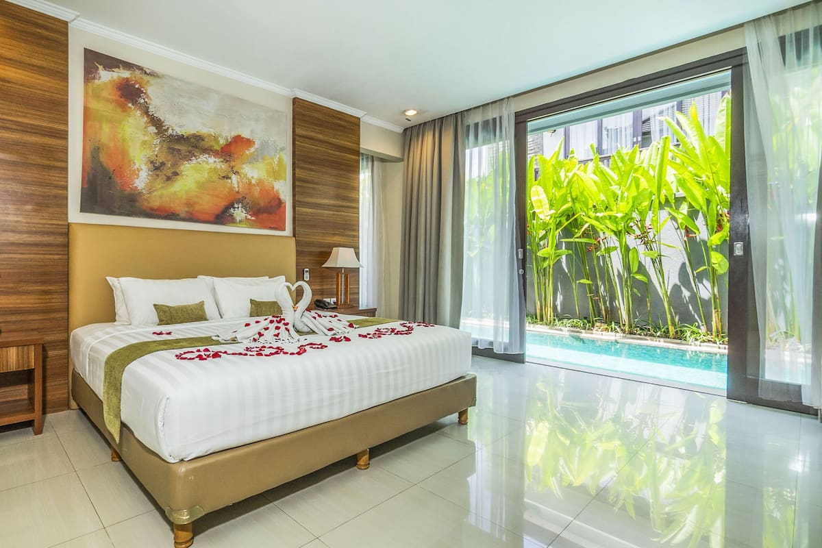 A spacious hotel room with a large bed, two bedside tables, a painting, and a view of a swimming pool.