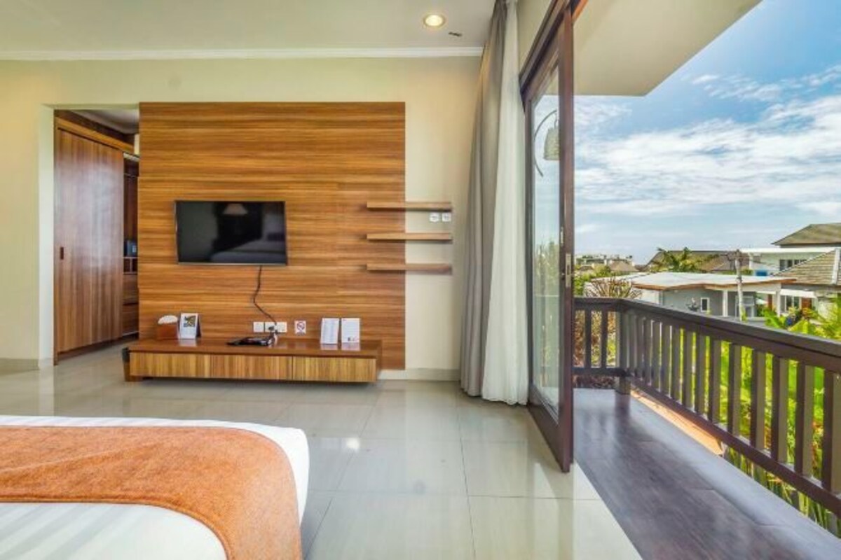 Une chambre d’hôtel moderne avec un téléviseur fixé sur un mur en panneaux de bois, un balcon avec vue et un lit parfaitement fait.