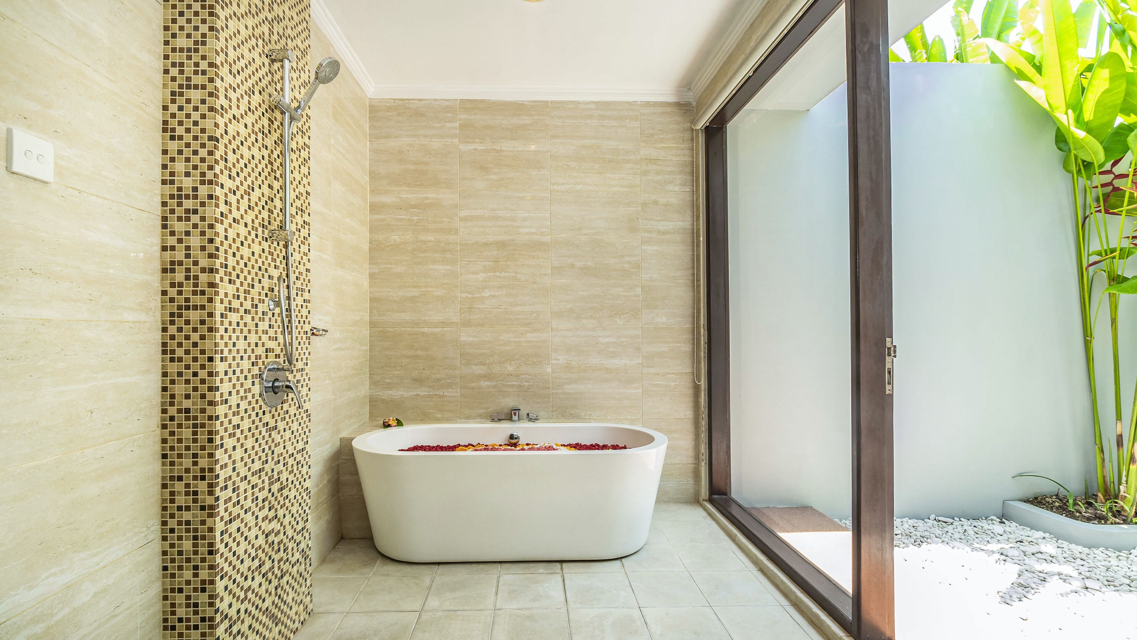 Un baño moderno con una bañera independiente, paredes con azulejos y un amplio ventanal con vistas a zonas verdes.