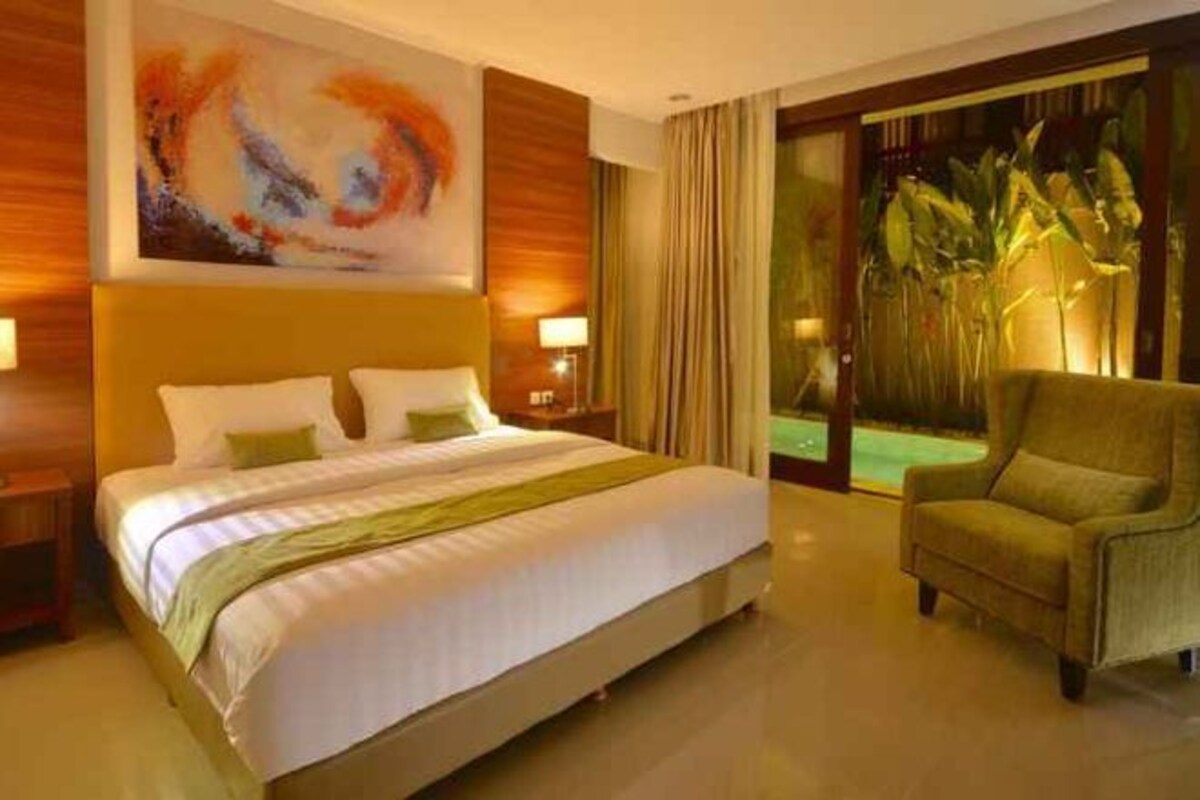 Une chambre d’hôtel avec un grand lit, un canapé, un tableau au mur et une vue sur un jardin.