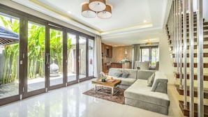 A modern living room with a sofa, coffee table, and a view of the outdoor garden. - Sotis Villa Canggu (Canggu)
