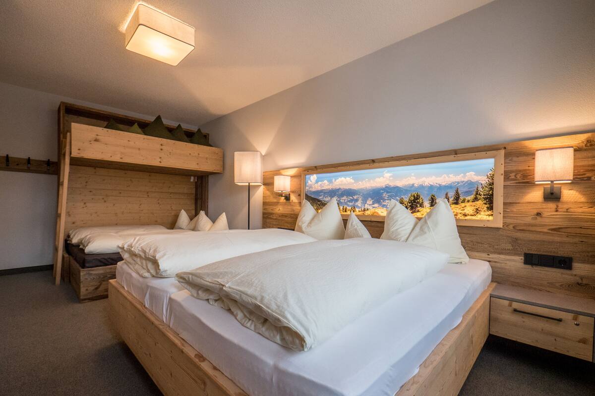 Ein Zimmer mit zwei Betten, Holz-Kopfteilen und einem großen Fenster mit Blick auf die Berge.