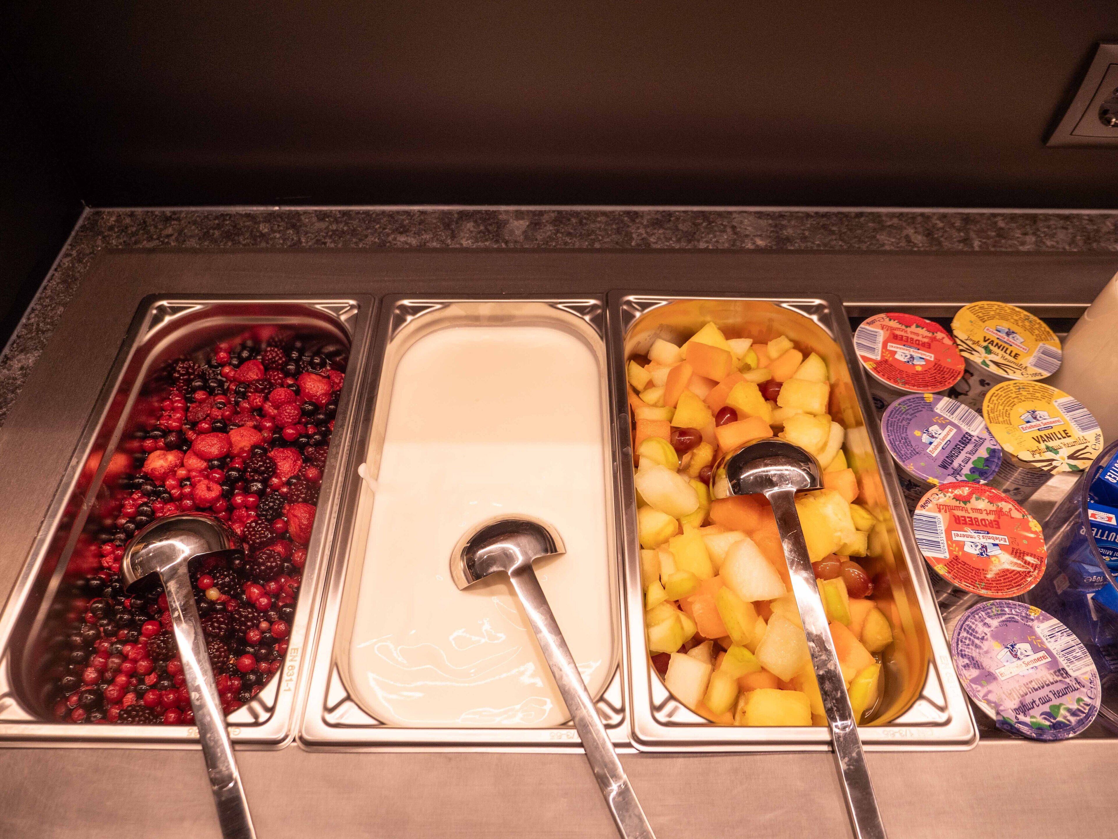 Un bufé con tres fuentes de comida, una con bayas, una con fruta y otra con yogur.
