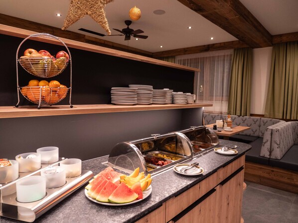 A buffet setup with various food items, a seating area with a sofa, and a ceiling fan. - Hotel & Apart Central (Fuegen)