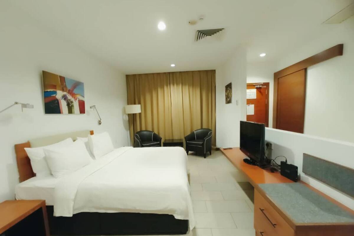 A hotel room with a bed, two chairs, a TV, a desk, and a large mirror.