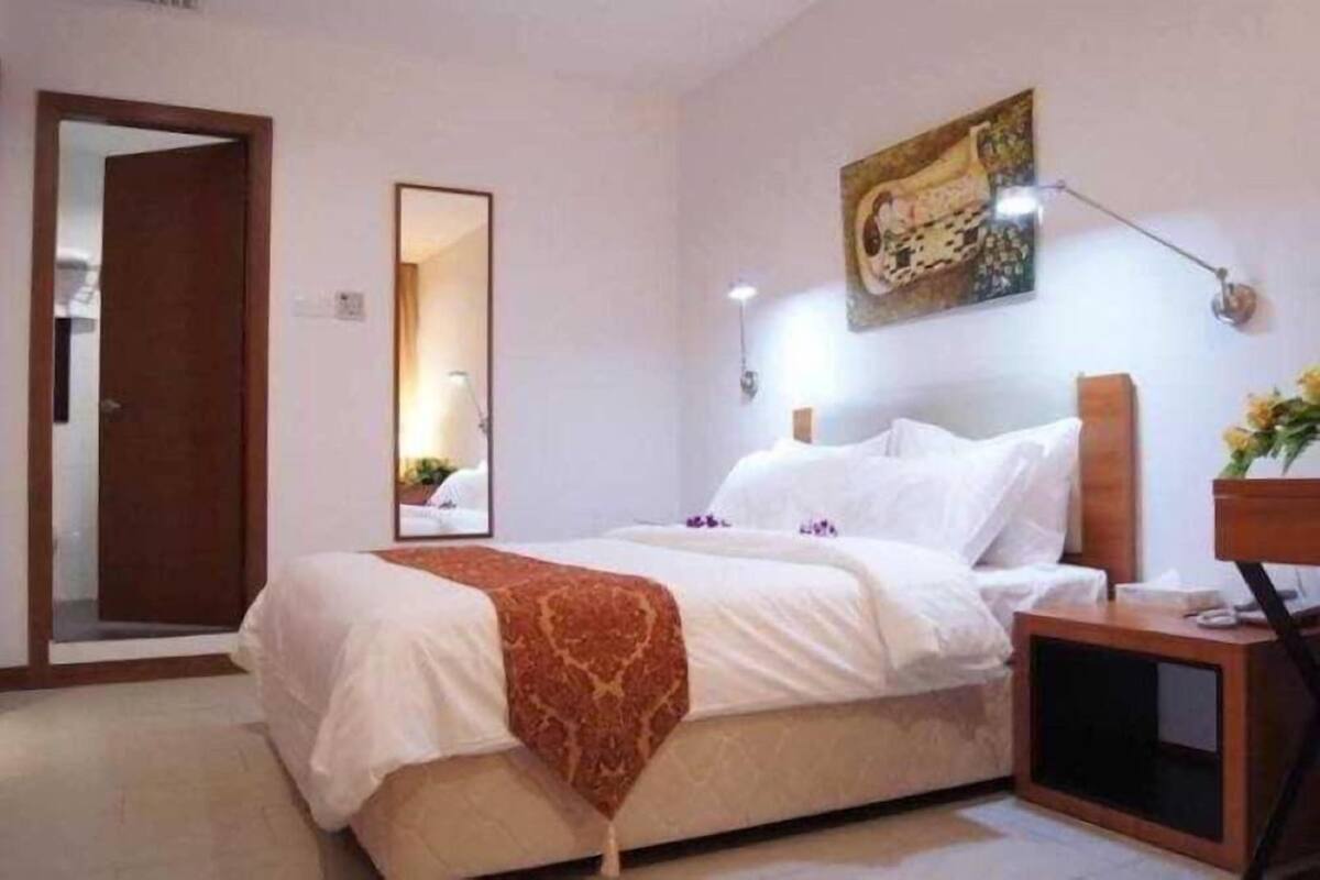 A hotel room with a bed, a bedside table, a mirror, and a painting on the wall.
