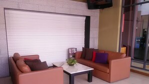 Un área de descanso con dos sofás y una mesa de centro, una ventana cerrada con persiana blanca y un televisor montado en la pared.