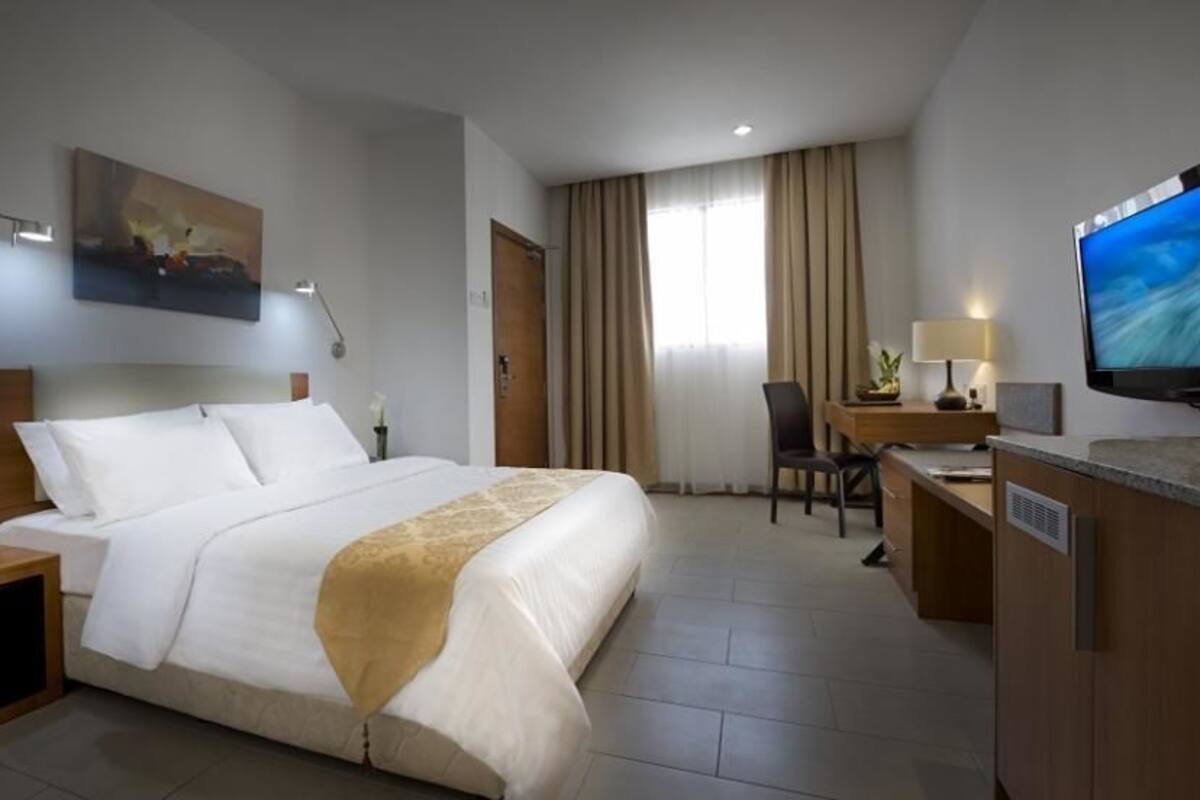A hotel room with a bed, desk, chair, television, and artwork on the wall.