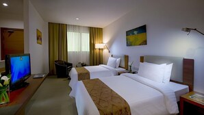Habitación de hotel con dos camas, un escritorio con computadora, televisor y ventana con cortinas.