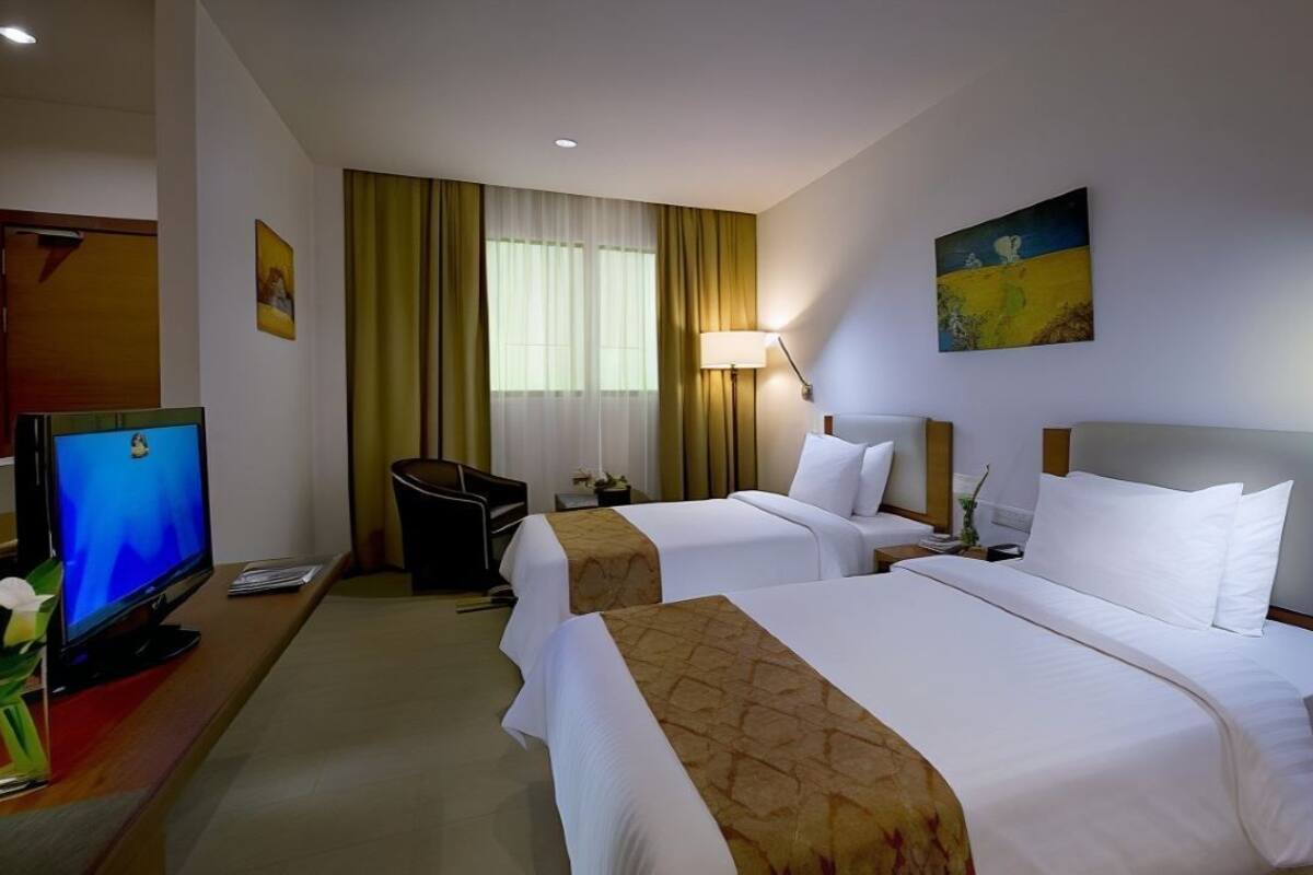 A hotel room with two beds, a desk with a computer, a TV, and a window with curtains.