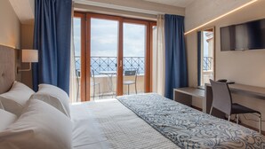 A hotel room with a bed, a desk, a chair, a TV, and a balcony with a view of the sea. - Hotel La Grotta (San Marino)