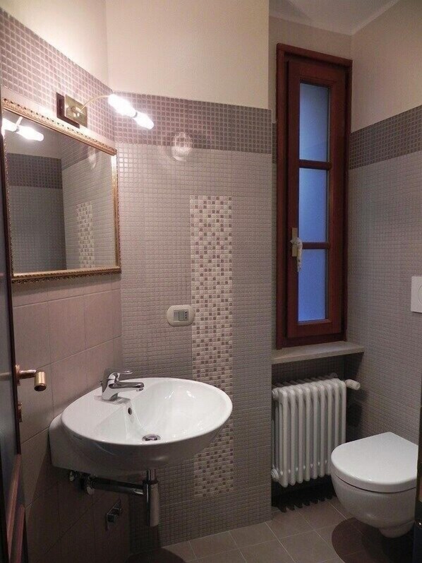 A bathroom with a white sink, a mirror, a window, and a toilet. - Hotel La Grotta (San Marino)