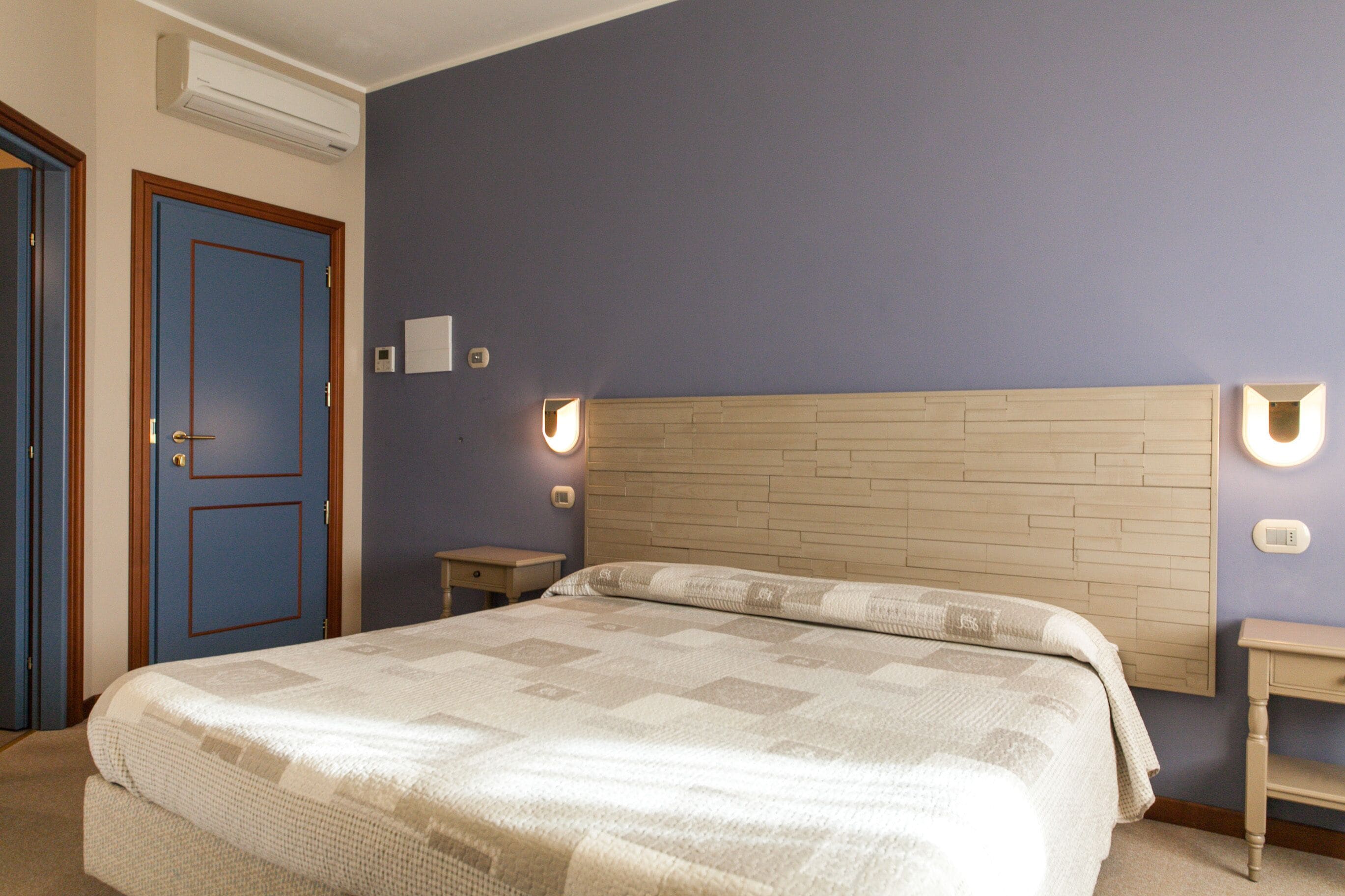 Une chambre à coucher comprenant un lit, une tête de lit en bois, une table de chevet et un luminaire fixé au mur.
