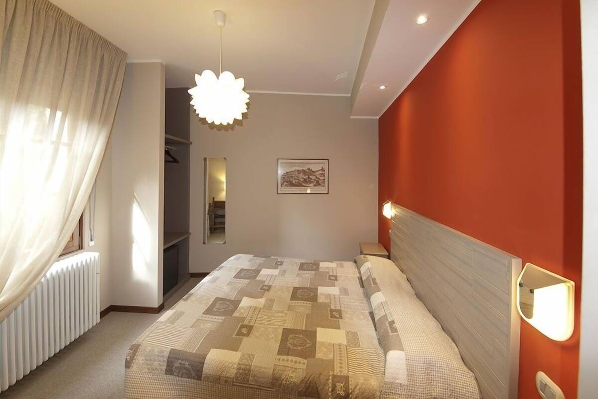 A bedroom with a large bed, a radiator, a mirror, and a wall-mounted light fixture.