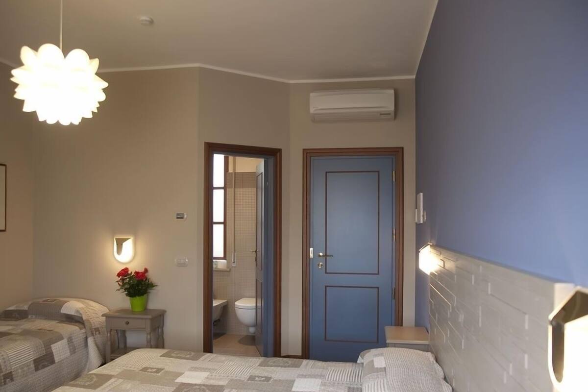A bedroom with a bed, a nightstand, a wall-mounted lamp, and a door leading to a bathroom.