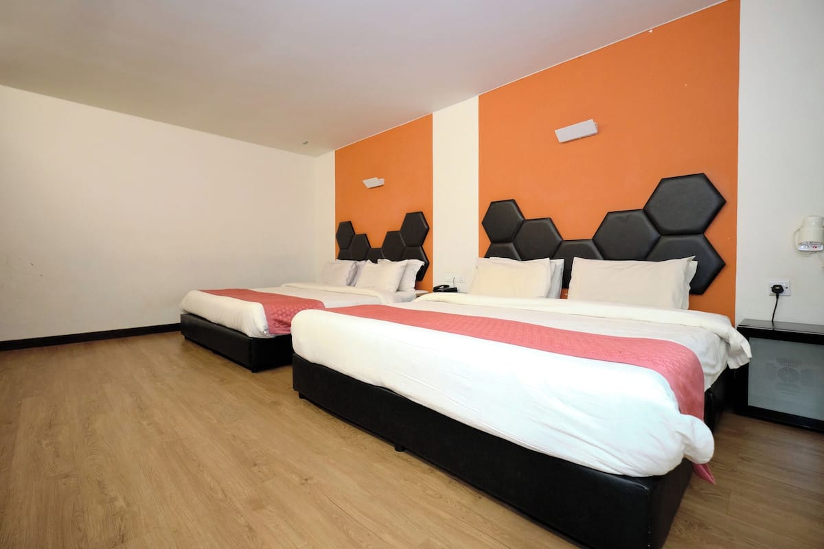 A hotel room with two beds, wooden flooring, and orange accent walls.