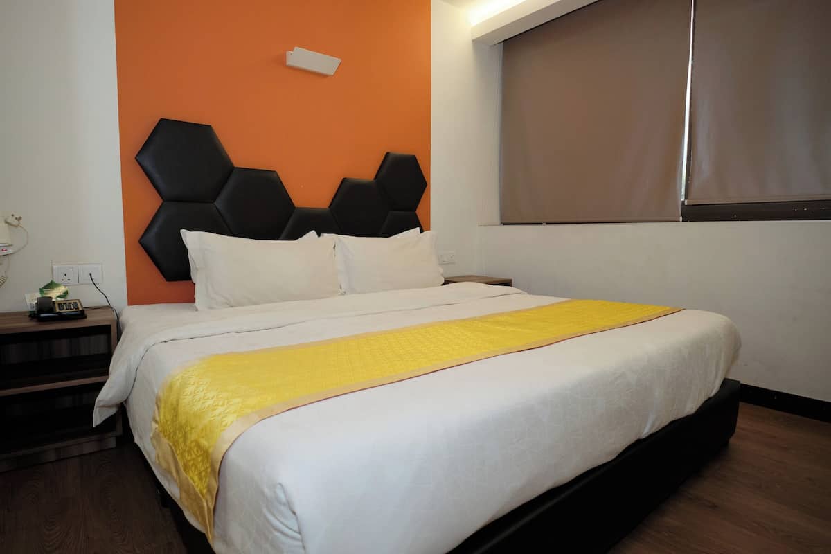 A neatly made bed with a white and yellow bedspread, a black headboard, and a window with a brown blind.