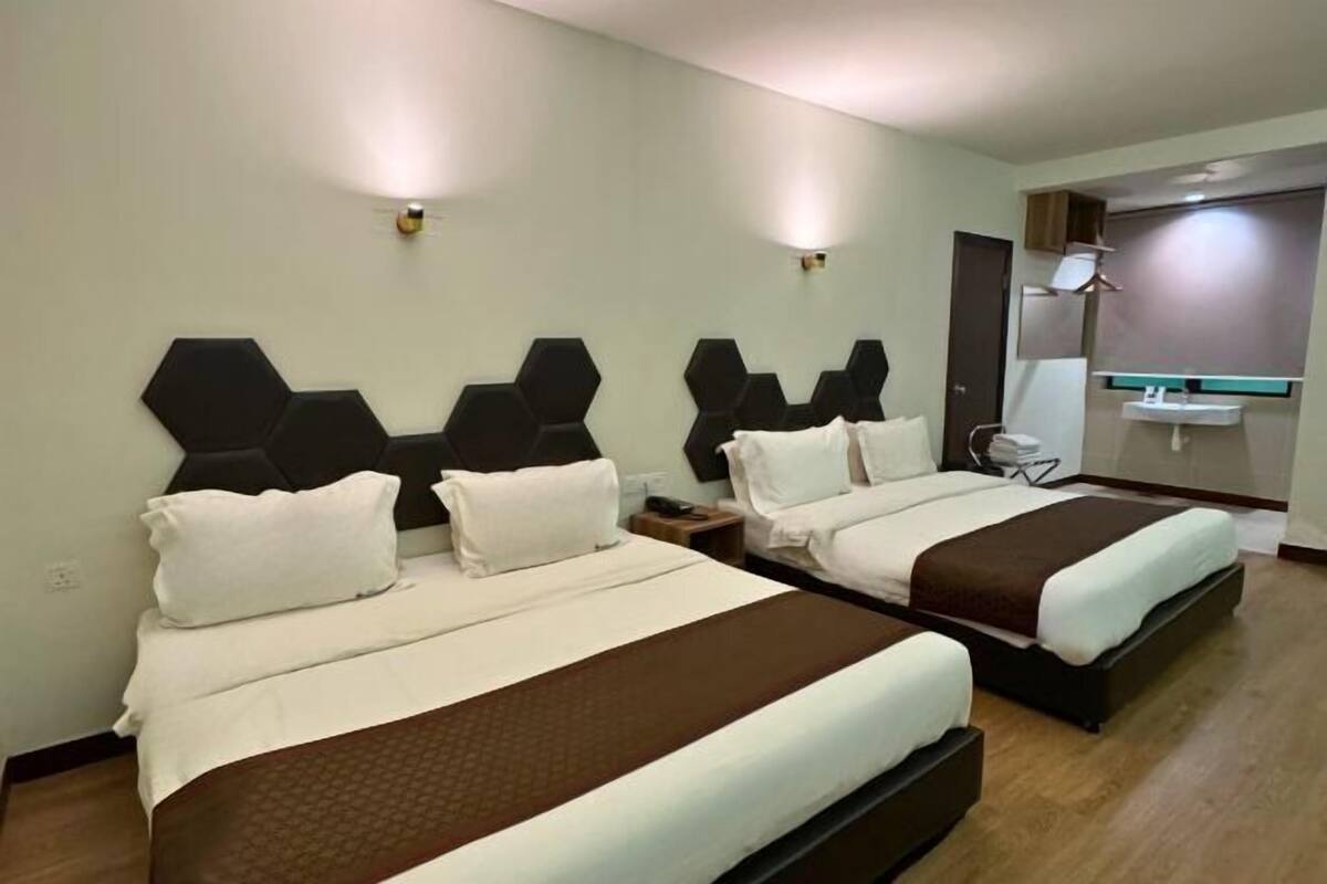 A hotel room with two beds, a bedside table, a nightstand, a mirror, and a bathroom with a sink and toilet.