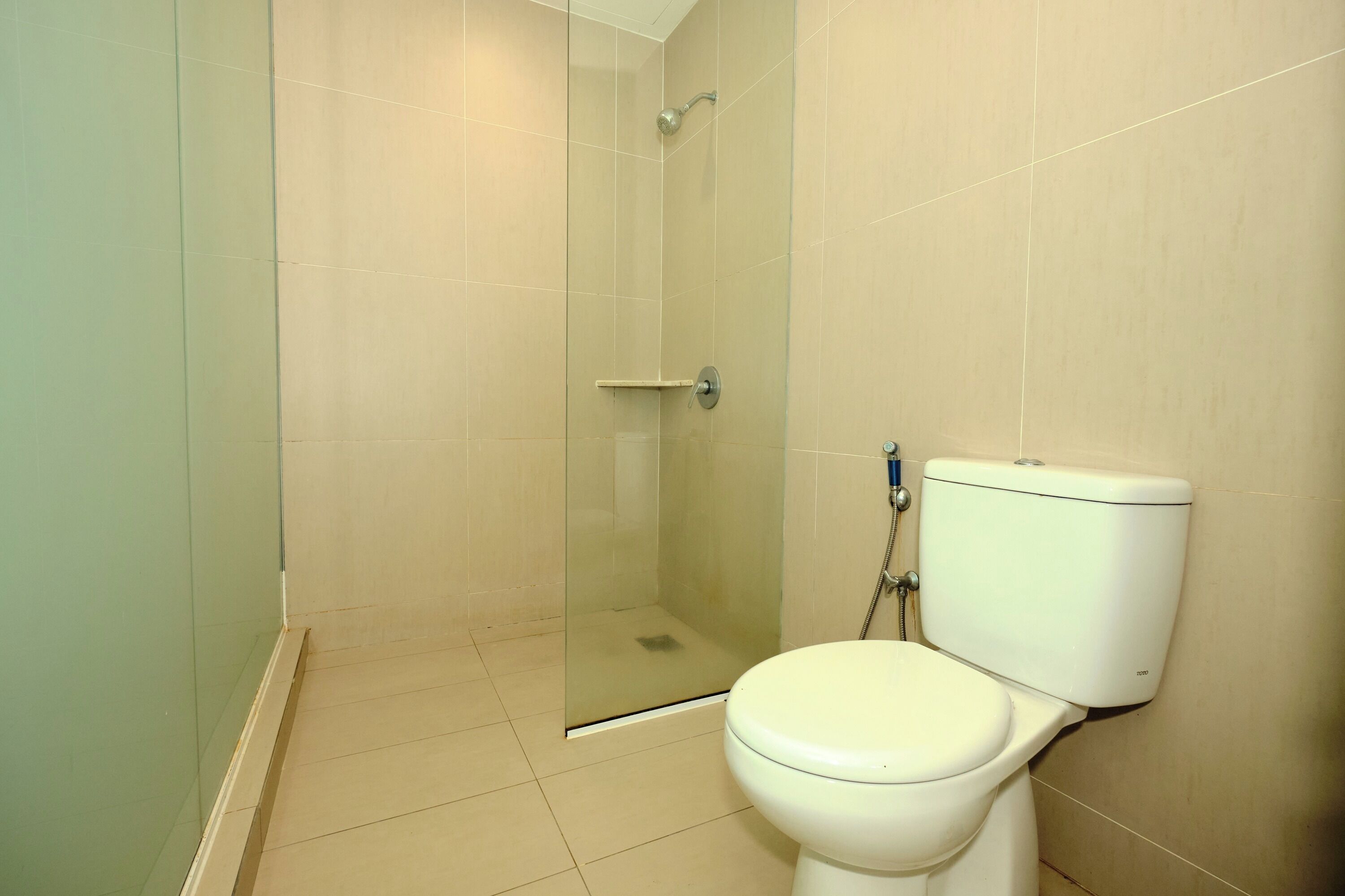 A bathroom with a toilet, a glass-enclosed shower, and beige tiled walls.
