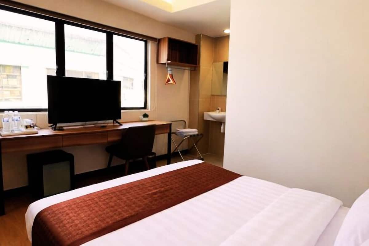 A hotel room with a bed, a desk with a television, a chair, a small table, and a window.
