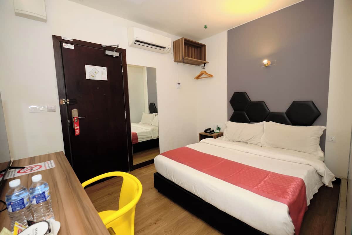 A hotel room with a bed, a wooden desk, a chair, a wardrobe, and a mirror.