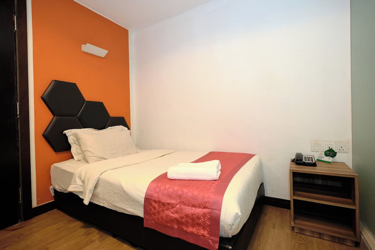 A neatly made bed with a white and red bedspread, a wooden nightstand with a phone and a green sign, and a black hexagonal headboard.