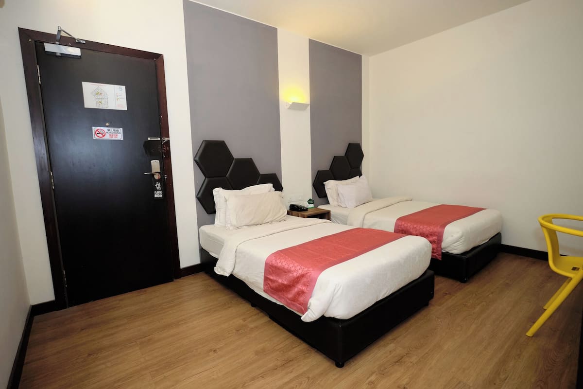 A hotel room with two beds, a wooden floor, a door with a sign, and a yellow chair.