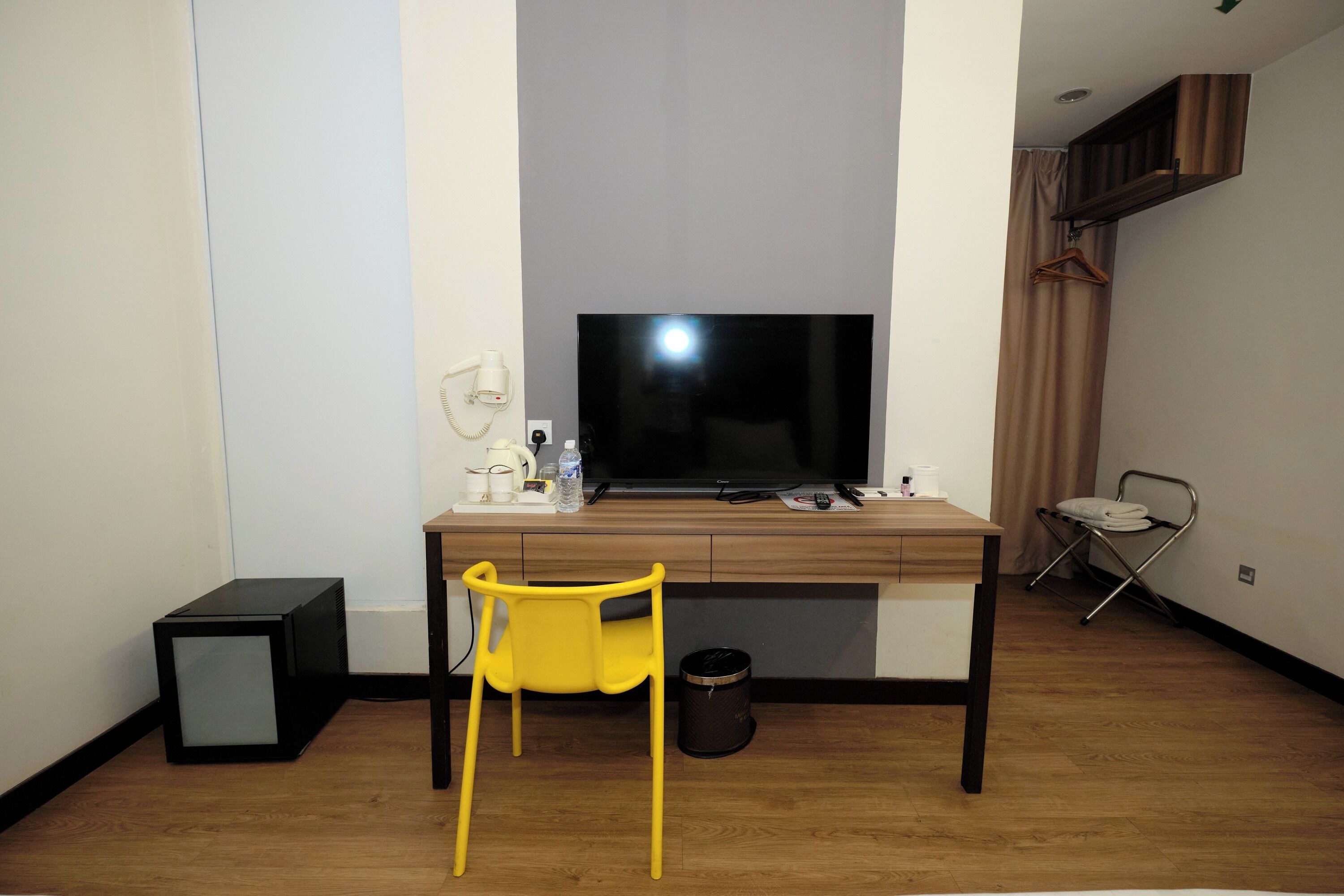 A small room with a wooden desk, a yellow chair, a television, and a small black speaker.