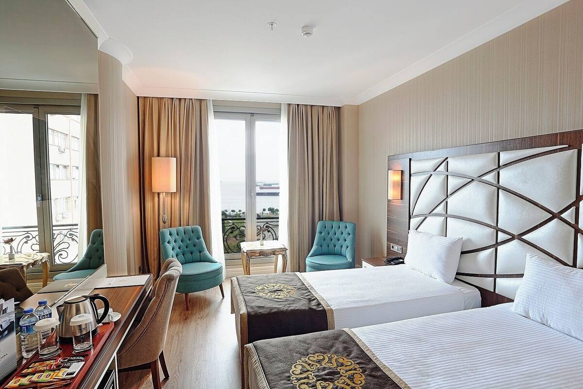 A hotel room with a large bed, two armchairs, a desk with a coffee maker, and a view of the city.