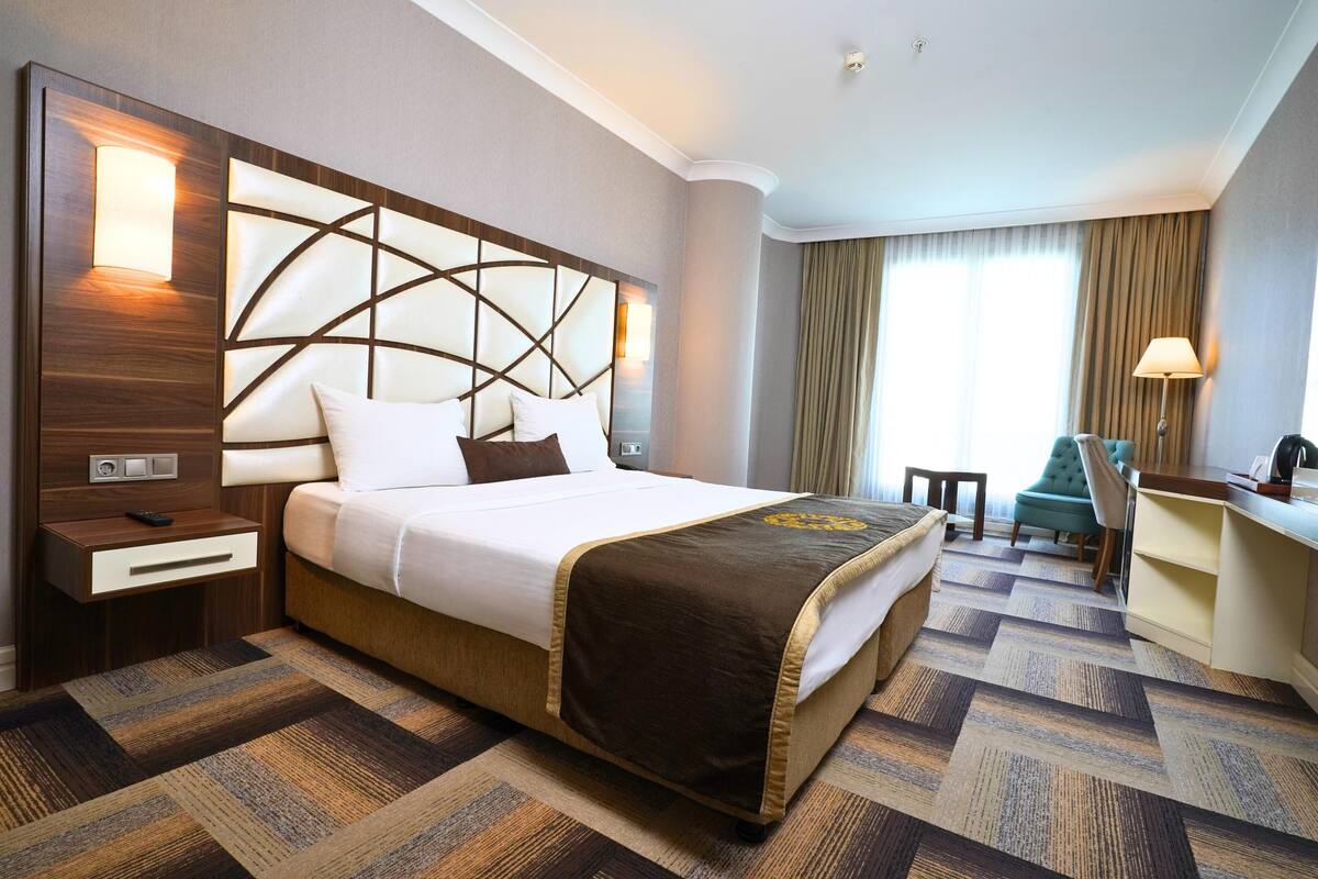 A hotel room with a large bed, a desk, a chair, and a view of the outdoors.
