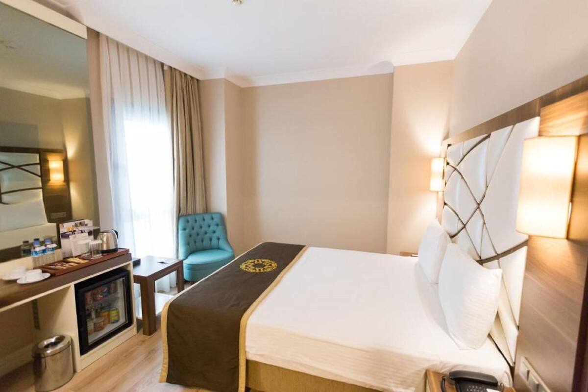 A hotel room with a bed, a desk with a minibar, a chair, and a large mirror.