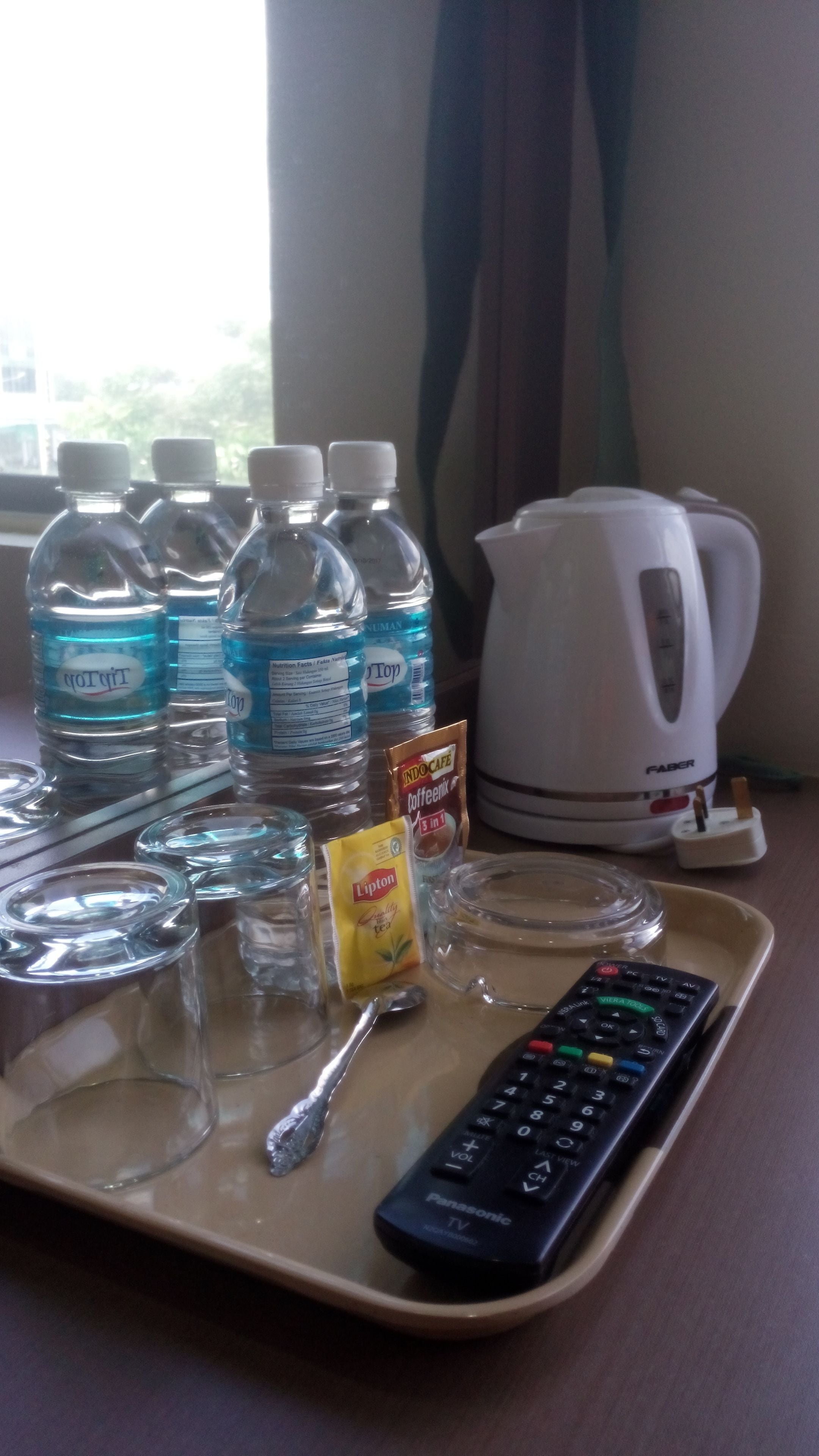 Una bandeja con un control remoto, una bolsita de té Lipton, una cuchara y varias botellas de agua sobre una mesa.